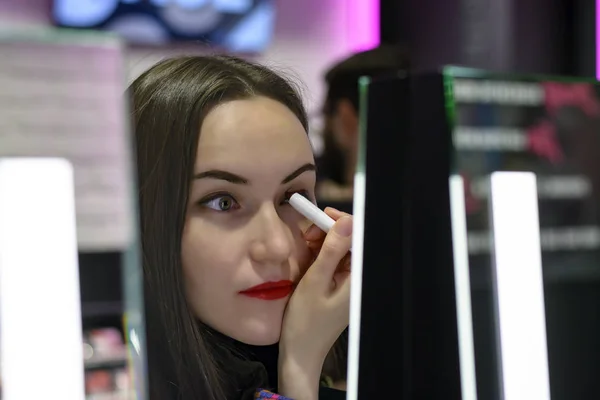 Mooie brunette met rode lippenstift is het testen van de eyeshadows in schoonheid winkel — Stockfoto