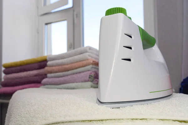 Ironing linen with steam generator. A stack of ironed towels lying next to the iron. Teflon sole plate covered with small holes