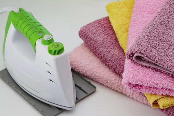 Ironing linen with steam generator. A stack of ironed towels lying next to the iron. Teflon sole plate covered with small holes