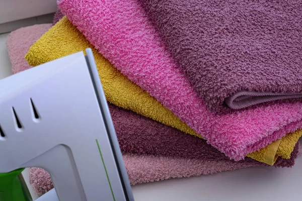 Ironing linen with steam generator. A stack of ironed towels lying next to the iron. Teflon sole plate covered with small holes — Stock Photo, Image
