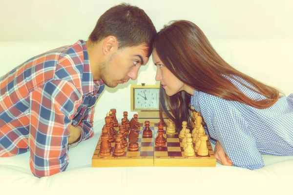 Relaxed young couple playing chess at home lying on sofa.