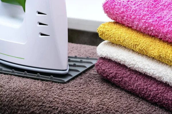 Ironing linen with steam generator. A stack of ironed towels lying next to the iron. Teflon sole plate covered with small holes