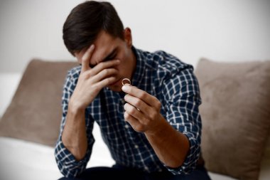 Boşanma kavramı. Nişan yüzüğü evde oturan tutan üzgün bir yalnız adam. Bir boşanma sonrası depresyon. Seçici odak.