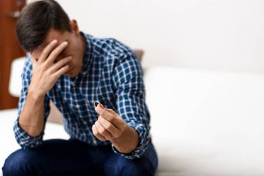 Boşanma kavramı. Nişan yüzüğü evde oturan tutan üzgün bir yalnız adam. Bir boşanma sonrası depresyon. Seçici odak.