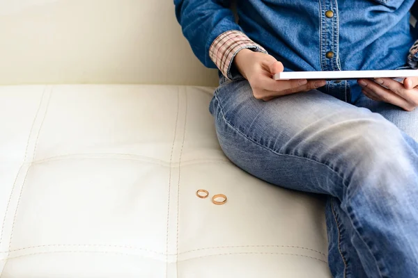 Sad woman after the divorce, looking at a family photo in the frame sitting on the floor near the sofa in the room. Concept of divorce