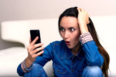 Onun baş ve Smartphone-e doğru görünüyor tutan genç kadın. Şok katta oturan.