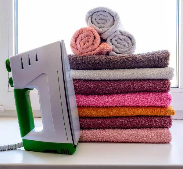 Ironing linen with steam generator. A stack of ironed towels lying next to the iron. Teflon sole plate covered with small holes