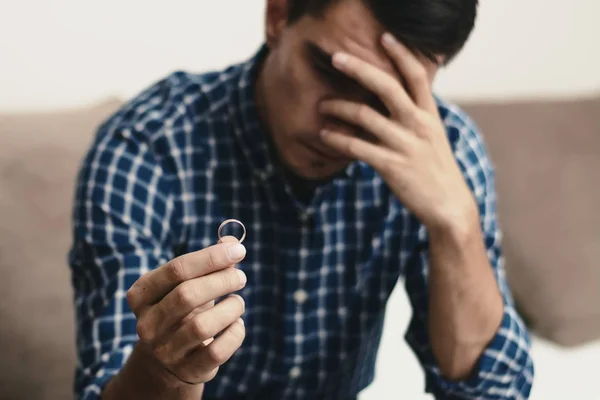 Boşanma kavramı. Nişan yüzüğü evde oturan tutan üzgün bir yalnız adam. Bir boşanma sonrası depresyon. Seçici odak.