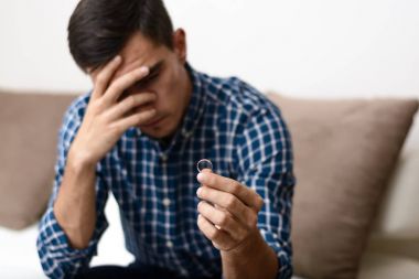 Boşanma kavramı. Nişan yüzüğü evde oturan tutan üzgün bir yalnız adam. Bir boşanma sonrası depresyon. Seçici odak.