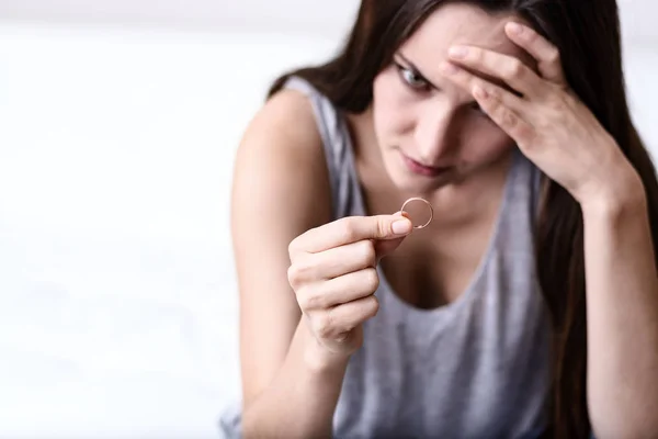 Enttäuschte Ehefrau nach Scheidung depressiv, hält Ehering auf weißem Sofa — Stockfoto