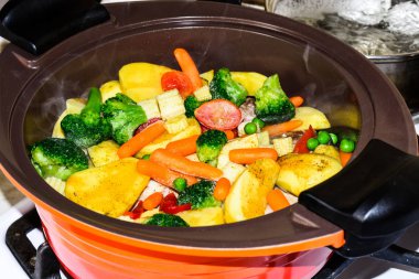 Sulu sebze yahni, turuncu bir seramik tencerede ocakta. Vejetaryenlik.