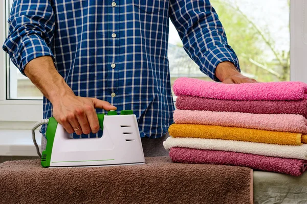 Hombre plancha ropa y toallas sobre tabla de planchar con plancha humeante blanco-verde . — Foto de Stock