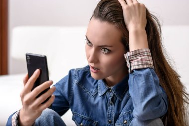 Onun baş ve Smartphone-e doğru görünüyor tutan genç kadın. Ne gördüğünü tarafından sıkıntılı