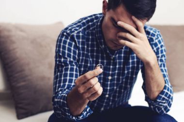 Boşanma kavramı. Nişan yüzüğü evde oturan tutan üzgün bir yalnız adam. Bir boşanma sonrası depresyon. Seçici odak.