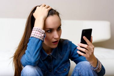 Onun baş ve Smartphone-e doğru görünüyor tutan genç kadın. Şok katta oturan.
