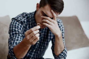 Boşanma kavramı. Nişan yüzüğü evde oturan tutan üzgün bir yalnız adam. Bir boşanma sonrası depresyon. Seçici odak.