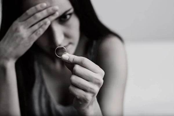 Esposa muy decepcionada y ofendida deprimida después del divorcio, sosteniendo con la mano un anillo de bodas sentado en el suelo de una habitación. Tonificación en blanco y negro . —  Fotos de Stock