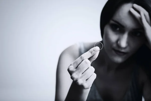 Esposa muy decepcionada y ofendida deprimida después del divorcio, sosteniendo con la mano un anillo de bodas sentado en el suelo de una habitación. Tonificación en blanco y negro . —  Fotos de Stock