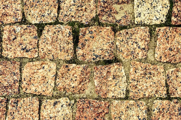 El pavimento de piedra. Textura de piedras en el primer plano de la carretera. Parte de un camino pavimentado con piedras cuadradas de granito rojo . — Foto de Stock