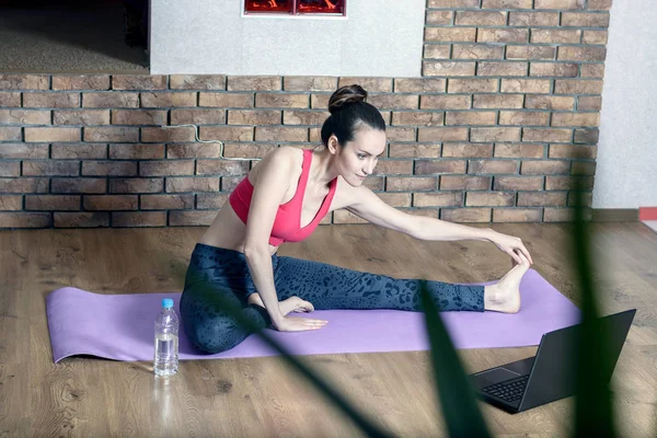 Young woman in sportswear is engaged in the home stretch on the floor while watching videos online — Stock Photo, Image