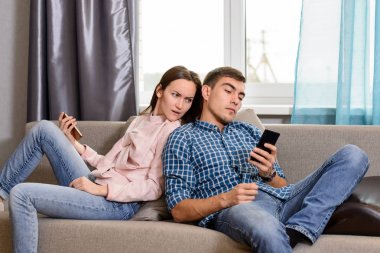 Genç çift kanepede oturan ve akıllı telefonlar kullanarak, karısı kocası casus telefonuna şüpheli
