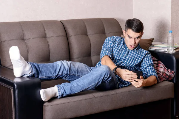 Retrato de un hombre sorprendido, se despertó en el sofá en casa y viendo en un teléfono inteligente, se quedó dormido para el trabajo, reunión, examen — Foto de Stock