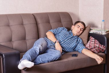 Genç bir adam kanepede televizyon izlerken uyuya.