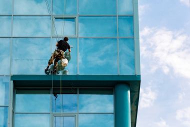 Endüstriyel tırmanışçı çamaşır ipinde asılı ve pencereleri yıkıyor, cam cephe modern bina