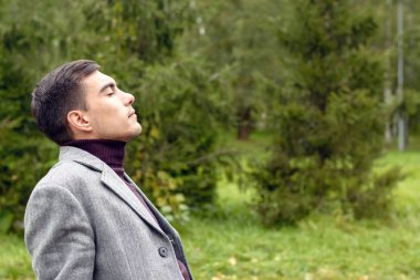 Yüzünü rüzgara gösterilen parkta sonbahar temiz havada nefes, gri bir ceket genç çekici adam portresi. Özgürlük, ekoloji, sınır tanımayan hayat kavramı