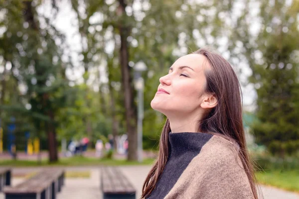 Retrato de una joven hermosa mujer que respira aire fresco de otoño en un parque verde. el concepto de aire atmosférico puro, el medio ambiente — Foto de Stock