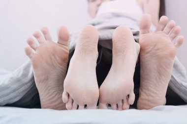 Çift yatakta eğleniyor. Çıplak ayak severler battaniyenin altından sopa dışarı.