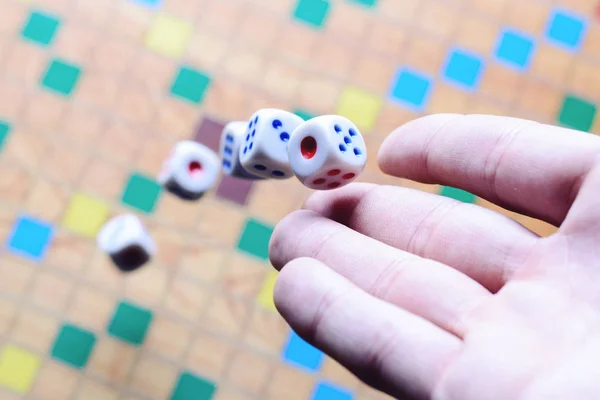 Hand werfen weiße Würfel Hintergrund bunte verschwommene Brettspiel. der dynamische Moment des Spiels, selektiver Fokus. — Stockfoto
