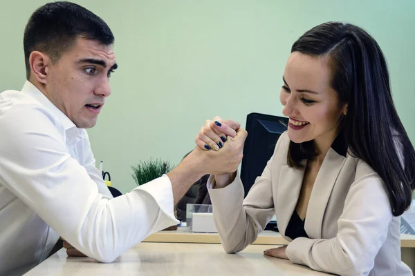 Young man and woman fight on his hands at the Desk in the office for a place Boss, head. The battle of the sexes, young couple having fun in the office. — Stock Photo, Image