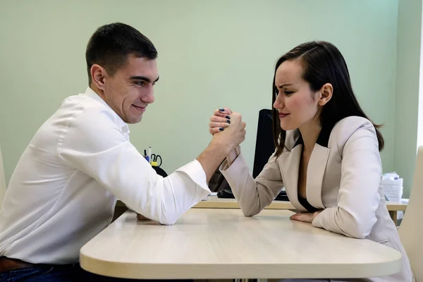 Young man and woman fight on his hands at the Desk in the office for a place Boss, head. The battle of the sexes, young couple having fun in the office. — Stock Photo, Image