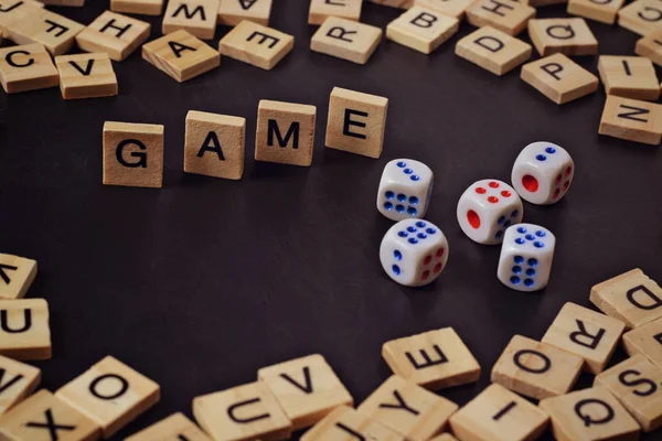 Kata GAME dengan huruf kayu di papan hitam dengan dadu dan huruf dalam lingkaran — Stok Foto