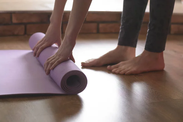 A barefoot woman twists a purple yoga Mat and fitness on the parquet floor — Stock Photo, Image