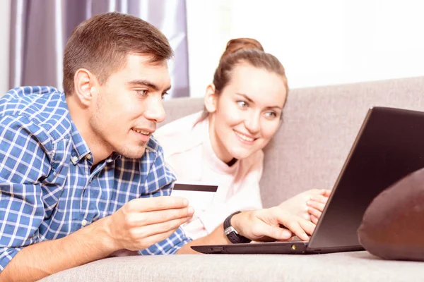 Modern young family makes purchases online Leda on sofa using a laptop, payment by credit card. Emotional face — Stock Photo, Image