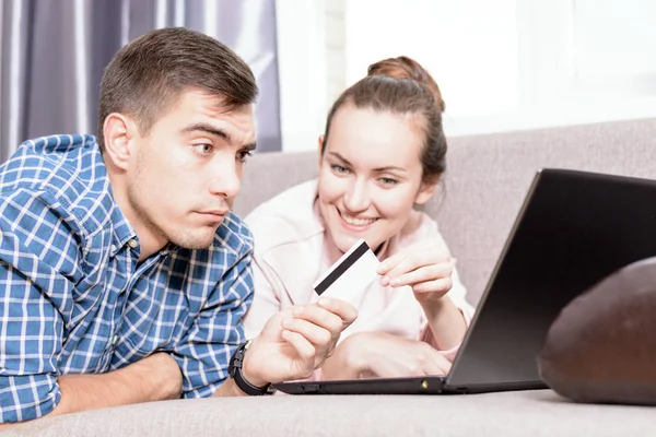 Modern young family makes purchases online Leda on sofa using a laptop, payment by credit card. Emotional face — Stock Photo, Image