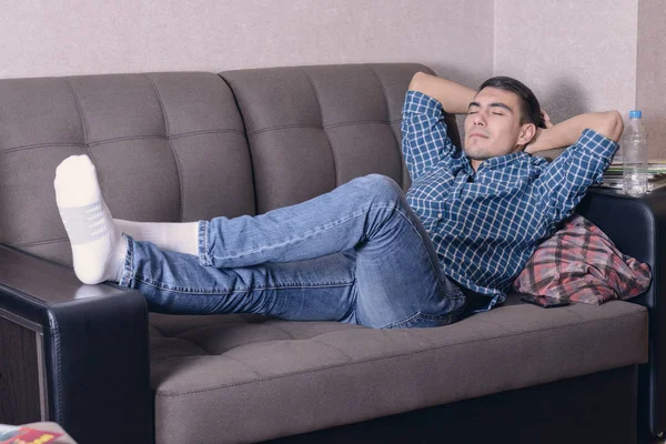 Despreocupado joven relajado en el sofá con las manos detrás de la cabeza, soñando con el futuro — Foto de Stock