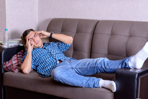 Joven acostado en el sofá sosteniendo la cabeza, dolores de cabeza . — Foto de Stock