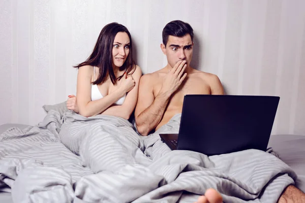 Young family couple using laptop and watching movies in bed. horror film — Stock Photo, Image