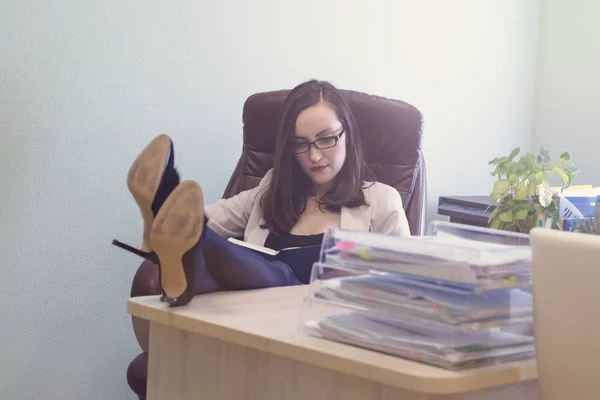 Женщина-офисный работник сидит в кожаном кресле, ноги на столе, учитывая план работы — стоковое фото