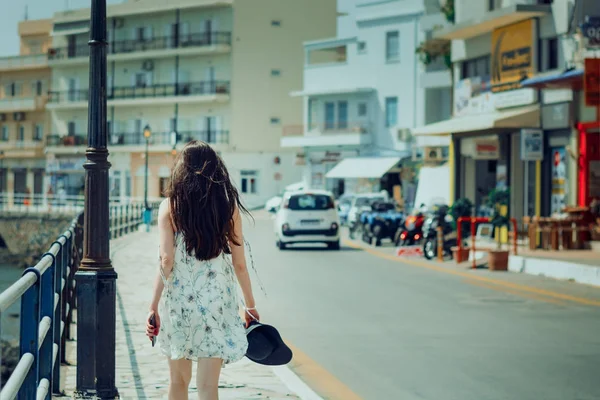 Молодая женщина с длинными темными волосами в белом сарафане ходит по улицам греческого города Агиос Николаос — стоковое фото