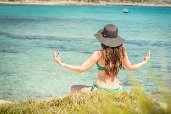 Jovem de fato de banho verde e chapéu preto pratica ioga na praia do mar Mediterrâneo. qigong e liberdade — Fotografia de Stock