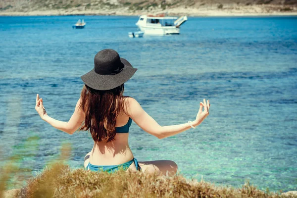 Jovem de fato de banho verde e chapéu preto pratica ioga na praia do mar Mediterrâneo. qigong e liberdade — Fotografia de Stock