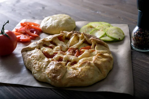 Frisch gebackene Galeta mit Gemüse und Käse auf einem Holztisch mit Zutaten, Olivenöl, Paprika, Tomaten und rohem Teig — Stockfoto