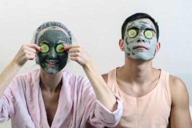 Yüzünde ve salatalık önünde kil maskeleriyle evli bir çift ön portresi. Spa evde. Cilt Bakımı