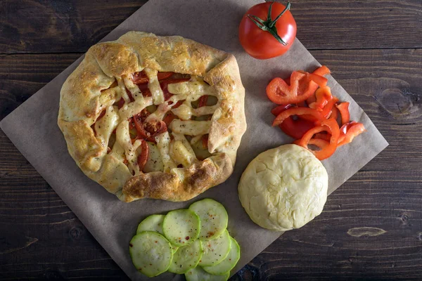Frisch gebackene Galeta mit Gemüse und Käse auf einem Holztisch mit Zutaten, Olivenöl, Paprika, Tomaten und rohem Teig — Stockfoto