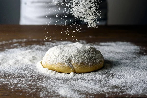 Raw dough ball sprinkled with white flour on a wooden table. Dynamically frozen flour in flight