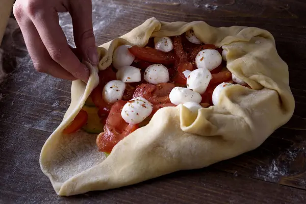 Frontansicht des Kochprozesses von Gemüsekeksen, Pizza. Frauenhände legen Mozzarella auf Tomaten und Zucchini auf einen ausgerollten Teig — Stockfoto